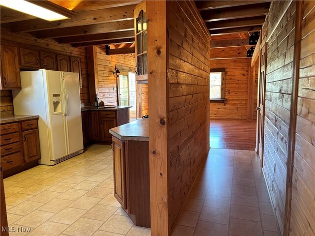 kitchen featuring white refrigerator with ice dispenser, wooden walls, and beam ceiling