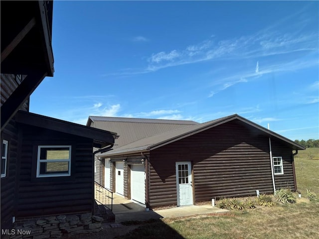 view of side of home featuring faux log siding, a garage, and metal roof