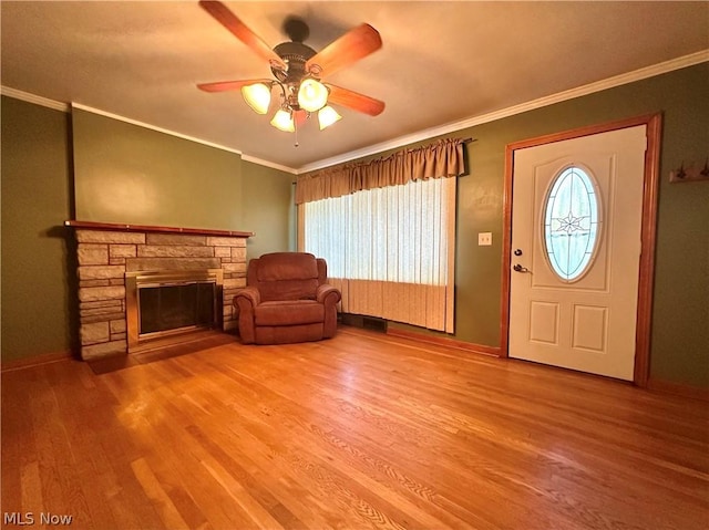 entryway with ceiling fan, hardwood / wood-style floors, ornamental molding, and a stone fireplace