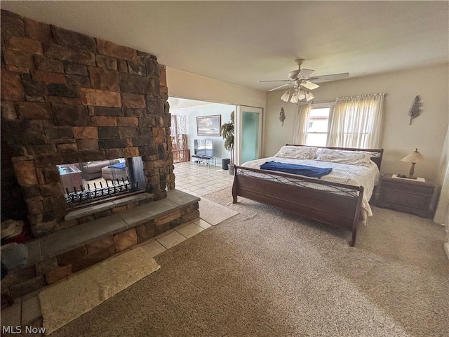 carpeted bedroom with ceiling fan and a stone fireplace