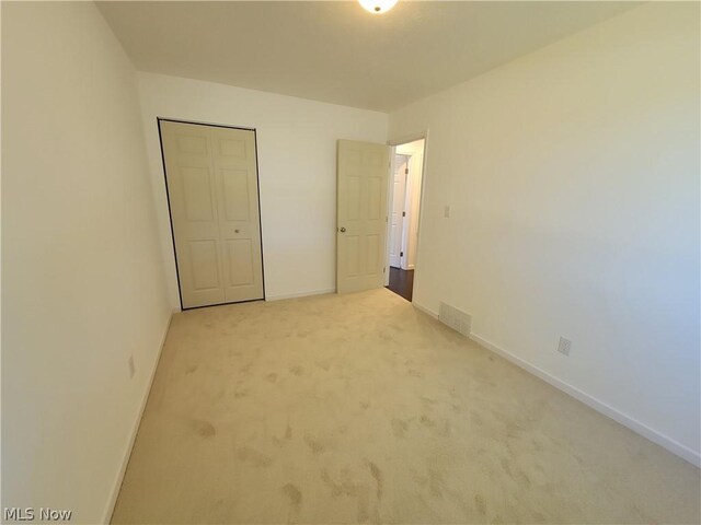 unfurnished bedroom with light carpet and a closet