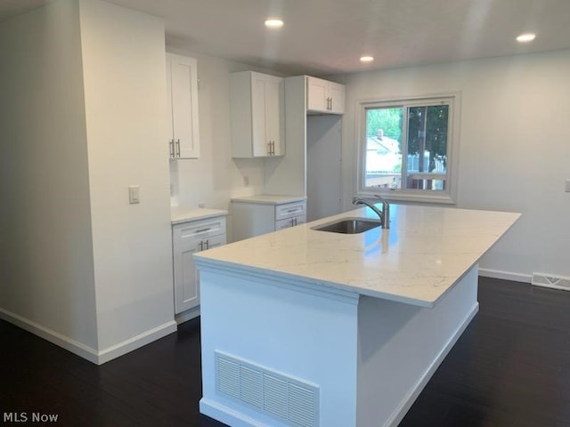 kitchen with white cabinetry, sink, light stone countertops, dark hardwood / wood-style flooring, and an island with sink