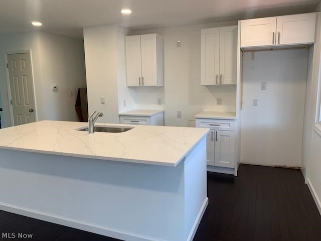 kitchen with light stone countertops, white cabinetry, sink, and an island with sink