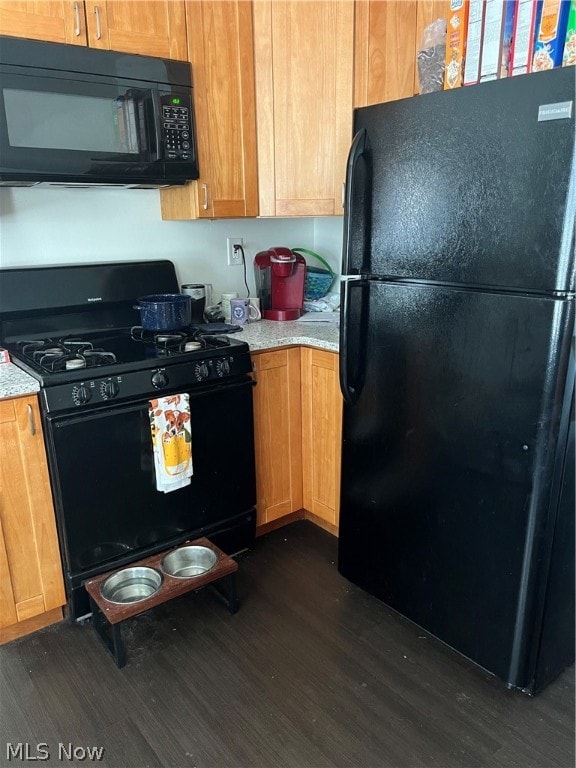 kitchen with black appliances, light stone counters, and dark hardwood / wood-style floors