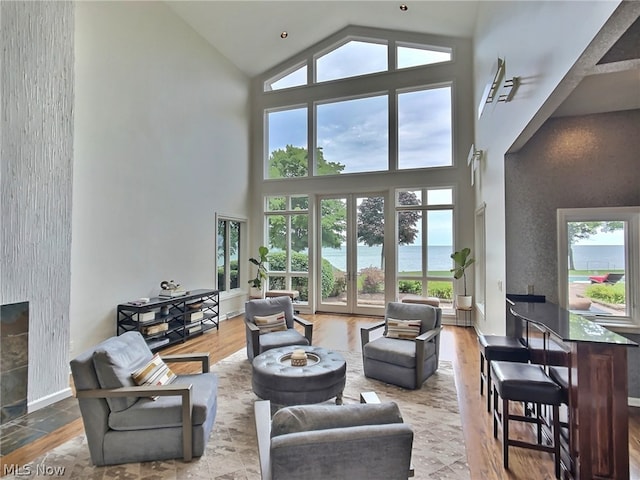 living room with a water view, hardwood / wood-style flooring, a tiled fireplace, and a high ceiling