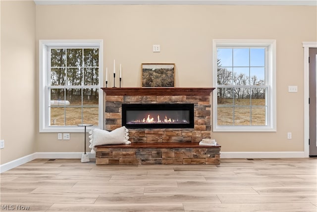 living room featuring light wood-type flooring, a stone fireplace, and plenty of natural light