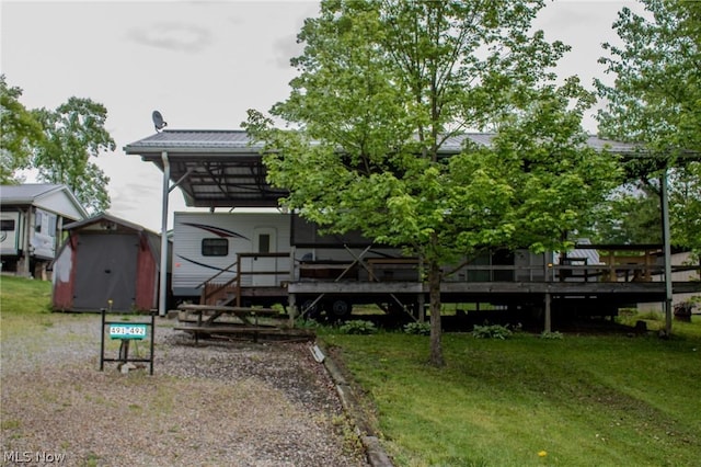 back of house with an outbuilding, a yard, a wooden deck, a carport, and a storage unit