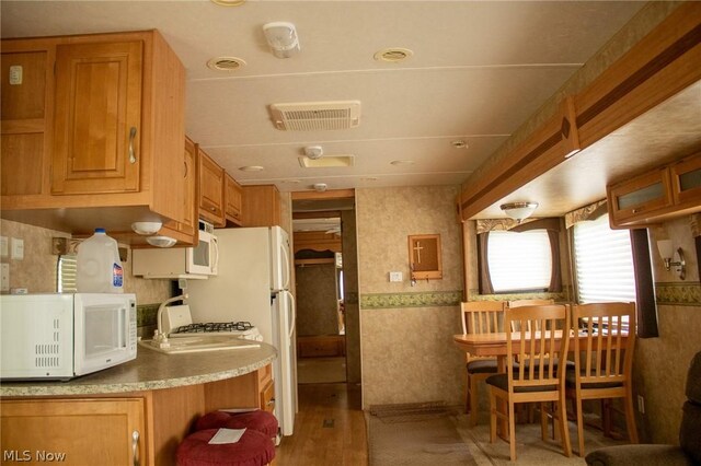 kitchen with visible vents, light wood finished floors, wallpapered walls, and white microwave