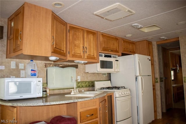 kitchen featuring white appliances, tasteful backsplash, visible vents, brown cabinetry, and a sink