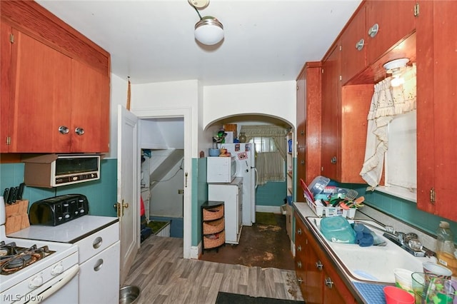 kitchen featuring arched walkways, white range with gas stovetop, a sink, light countertops, and dark wood finished floors