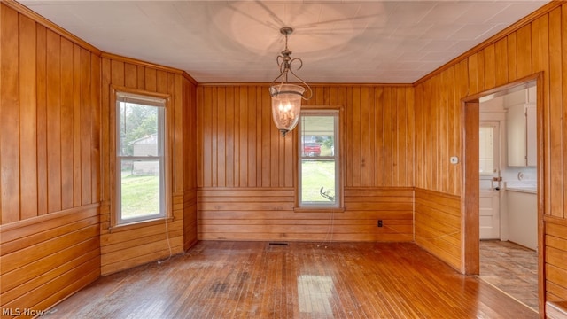 unfurnished dining area featuring hardwood / wood-style floors, a healthy amount of sunlight, and wood walls