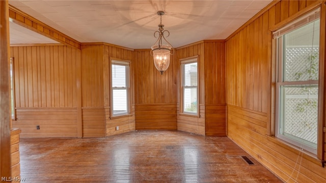 spare room featuring a chandelier, a healthy amount of sunlight, hardwood / wood-style floors, and wooden walls