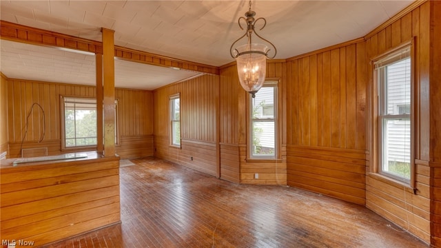 unfurnished dining area with plenty of natural light, wood-type flooring, wood walls, and an inviting chandelier