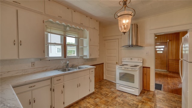 kitchen featuring hanging light fixtures, sink, white cabinets, white appliances, and wall chimney range hood