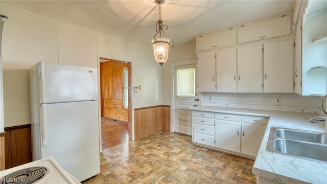 kitchen featuring white cabinetry, hanging light fixtures, white fridge, sink, and wood walls