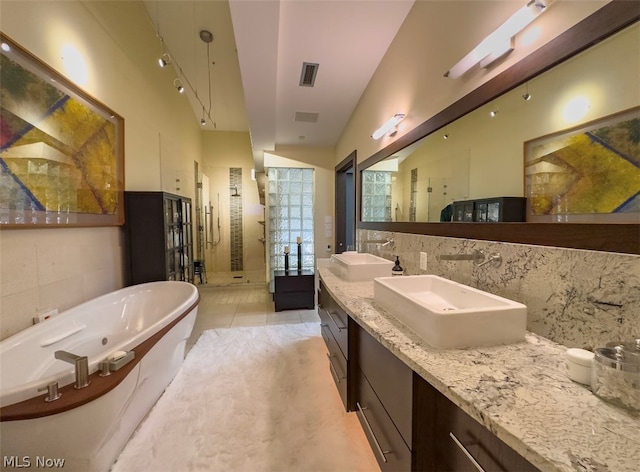 bathroom with vaulted ceiling, tile patterned flooring, tile walls, a tub, and double sink vanity