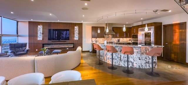 kitchen featuring built in appliances, light hardwood / wood-style flooring, tasteful backsplash, expansive windows, and wall chimney exhaust hood