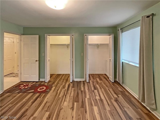 unfurnished bedroom with wood finished floors, baseboards, and two closets