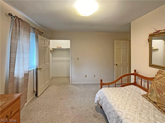 bedroom featuring light carpet, a spacious closet, and baseboards