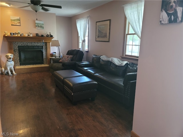 living room with a tiled fireplace, dark hardwood / wood-style flooring, and ceiling fan