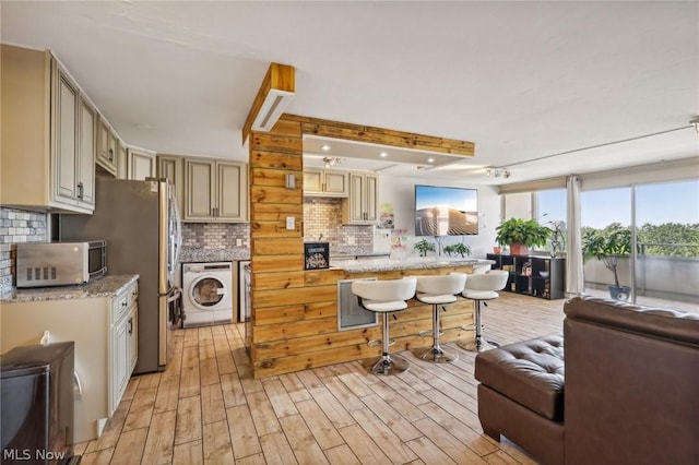 kitchen featuring washer / dryer, a kitchen bar, decorative backsplash, cream cabinetry, and light hardwood / wood-style flooring