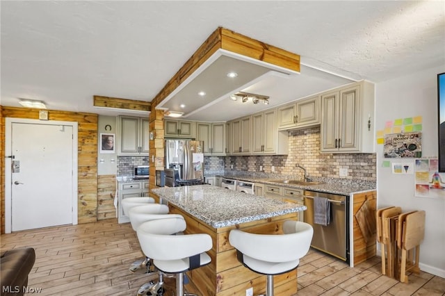 kitchen featuring appliances with stainless steel finishes, sink, backsplash, a center island, and light stone counters
