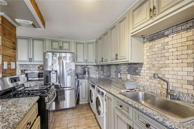 kitchen featuring appliances with stainless steel finishes, tasteful backsplash, sink, independent washer and dryer, and light hardwood / wood-style floors