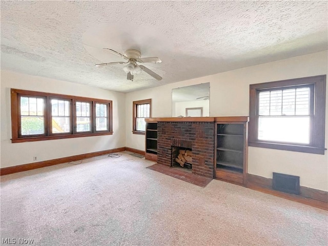 unfurnished living room with ceiling fan, a textured ceiling, a brick fireplace, and carpet flooring