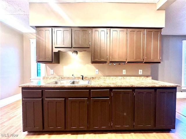 kitchen with dark brown cabinets, light hardwood / wood-style floors, light stone counters, and sink