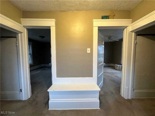 hall featuring dark carpet and a textured ceiling