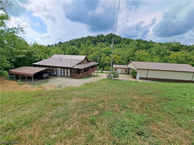 rear view of house with driveway, a view of trees, a lawn, an outbuilding, and an outdoor structure