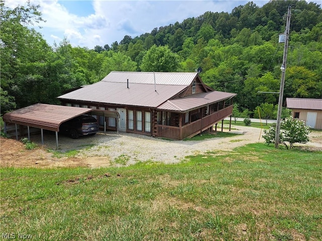 back of house with driveway, a forest view, metal roof, covered porch, and a yard