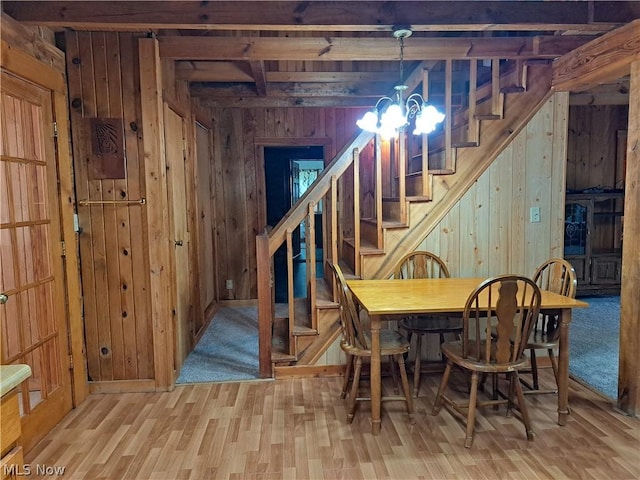 dining area with a chandelier, light wood-style flooring, wooden walls, stairway, and beamed ceiling