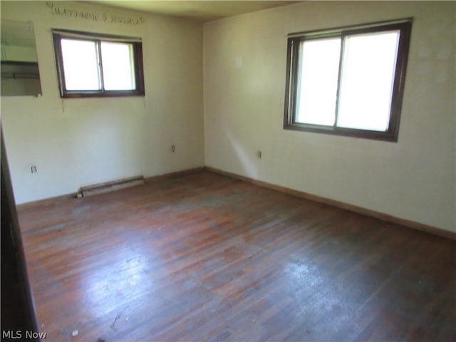 unfurnished room with hardwood / wood-style floors, a healthy amount of sunlight, and a baseboard heating unit