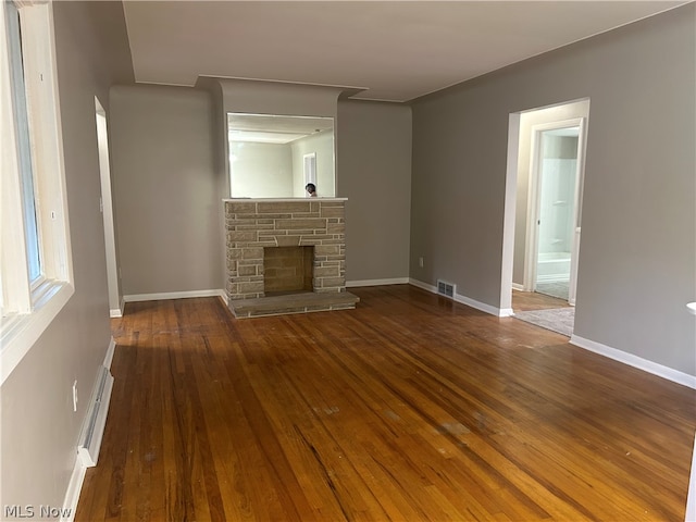 unfurnished living room featuring a stone fireplace, hardwood / wood-style flooring, and a baseboard heating unit