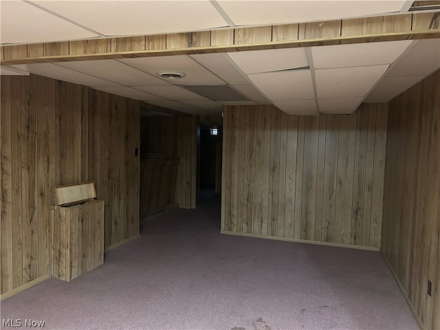 basement with carpet, wooden walls, and a drop ceiling