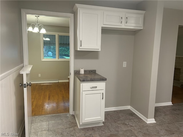 kitchen with white cabinetry, a notable chandelier, a baseboard radiator, and dark tile patterned flooring