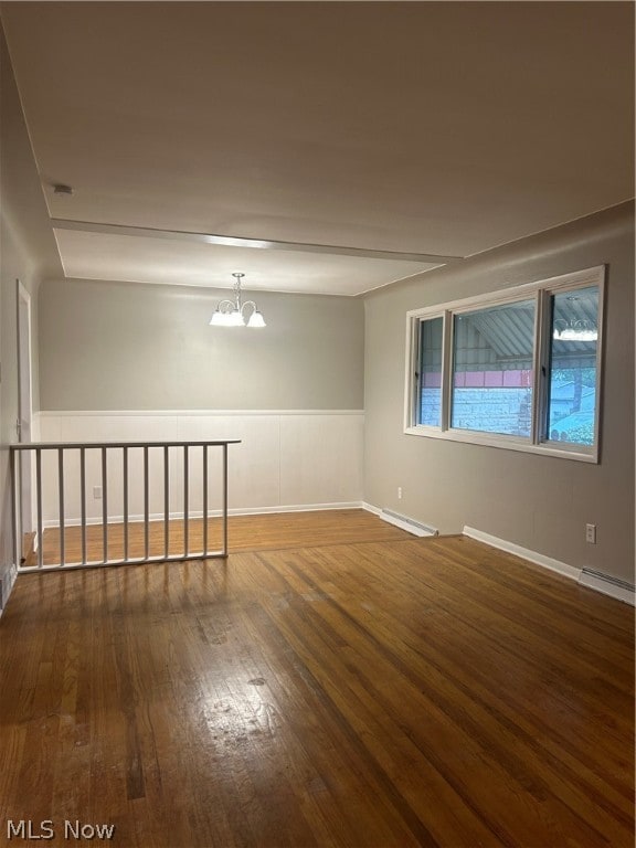 empty room featuring a chandelier, hardwood / wood-style flooring, and baseboard heating