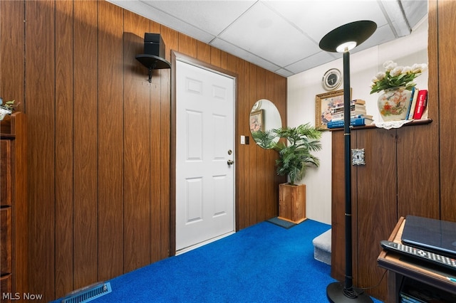 miscellaneous room with carpet floors, a paneled ceiling, and wood walls