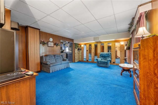 unfurnished living room with a drop ceiling, french doors, wooden walls, and carpet floors