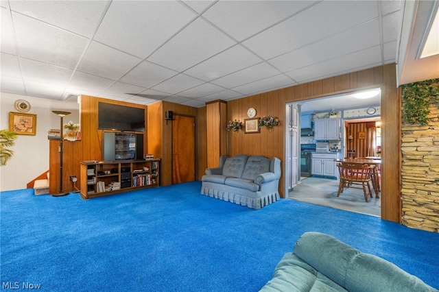 carpeted living room featuring wooden walls and a drop ceiling