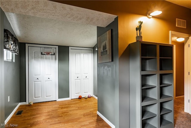 corridor with hardwood / wood-style flooring, a textured ceiling, and lofted ceiling