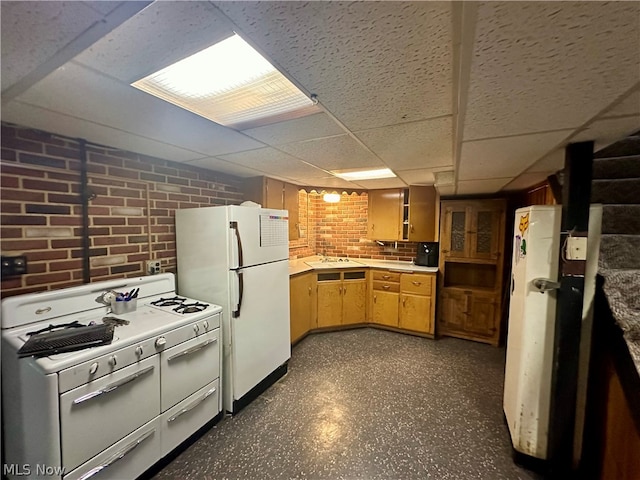 kitchen with white appliances, sink, light brown cabinets, a drop ceiling, and brick wall