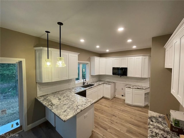 kitchen with light stone countertops, black microwave, a peninsula, a sink, and decorative backsplash