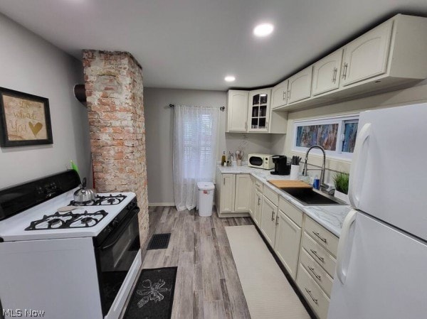 kitchen with light hardwood / wood-style flooring, white appliances, sink, white cabinetry, and brick wall