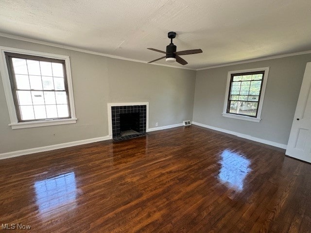 unfurnished living room with ceiling fan, a tiled fireplace, hardwood / wood-style flooring, and crown molding