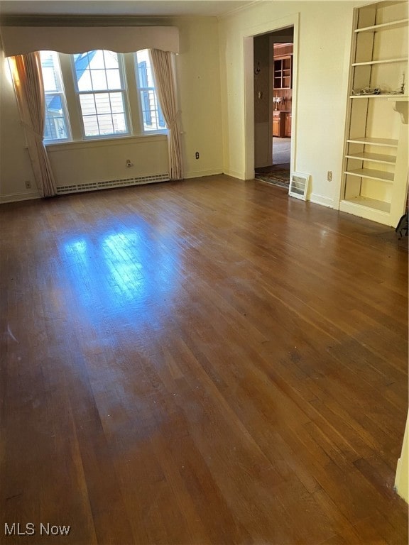 spare room featuring a baseboard radiator, dark wood-type flooring, and built in shelves