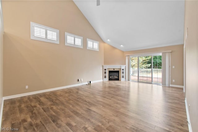 unfurnished living room with a tiled fireplace, hardwood / wood-style floors, and high vaulted ceiling