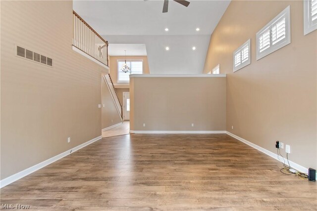 spare room featuring a high ceiling, ceiling fan with notable chandelier, and hardwood / wood-style flooring