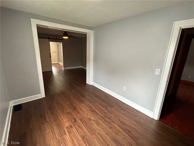 spare room with dark hardwood / wood-style floors, ceiling fan, and a barn door